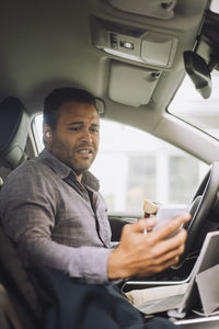 Worried male freelancer looking at mobile phone while sitting in car