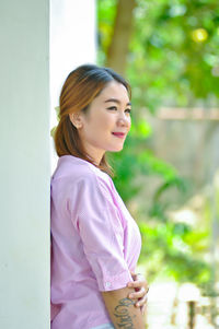 Smiling young woman looking away while standing by wall