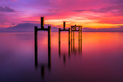 Wooden posts in sea against romantic sky at sunset