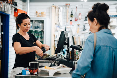 Cashier scanning paint brush while customer standing at checkout counter in hardware store