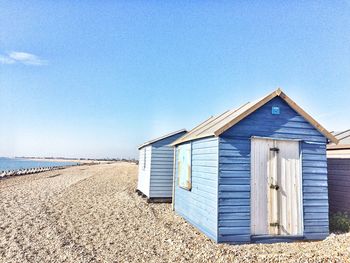 Hut on beach by sea against clear blue sky
