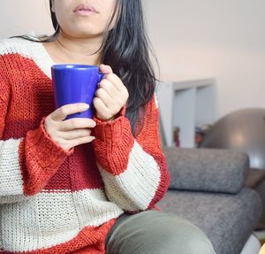 Midsection of woman having drink while sitting on sofa