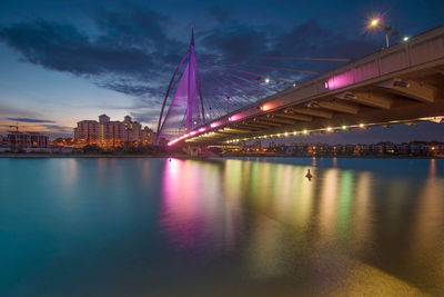 Bridge over lake against sky in city at dusk