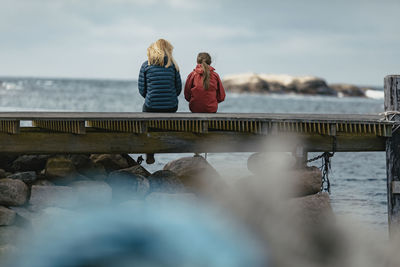 Woman sitting on railing by sea against sky