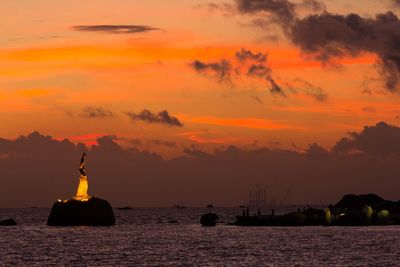 Silhouette sculpture by sea against sky during sunset