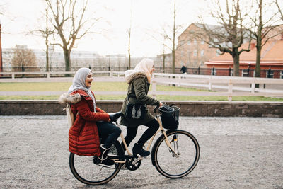 Side view of young woman riding bicycle with female friend on street