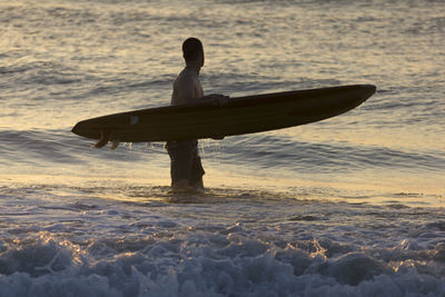 Silhouette man on shore against sky during sunset surfing 