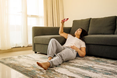 Woman relaxing on carpet, using phone, doing yoga, relaxing