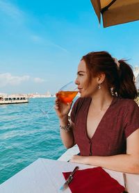 Young woman drinking juice looking at sea while sitting outdoors