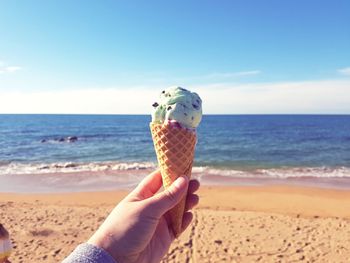 Hand holding ice cream cone on beach