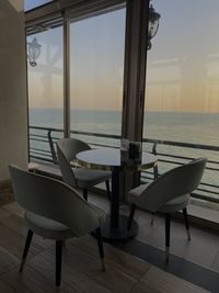 Empty chairs and tables in restaurant by sea against sky