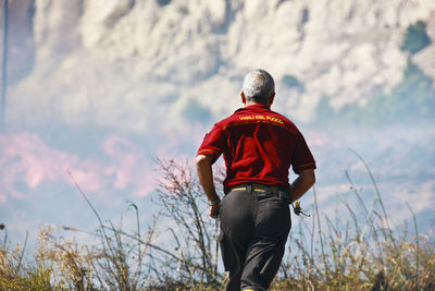 Rear view of man standing on mountain against sky