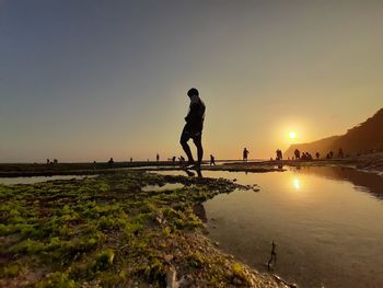 Man standing on shore against sky during sunset