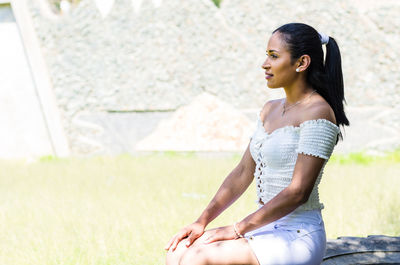 Side view of young woman sitting against wall