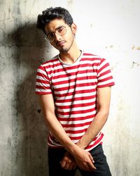 Young man looking away while standing against wall