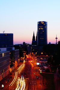 Traffic on city street by buildings against sky at night