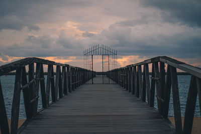 Pier on footbridge against sky during sunset