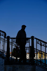 Silhouette man standing by railing against clear blue sky