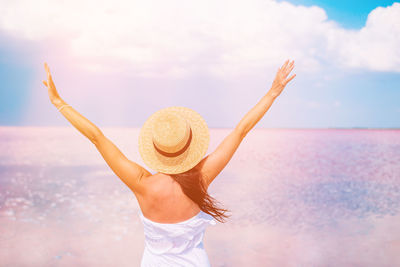 Rear view of woman wearing hat on beach against sky