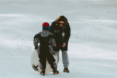 Beautiful woman by son with sled on snow covered field during winter