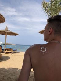 Rear view of shirtless man at beach against sky