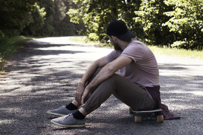 Man sitting on skateboard at footpath