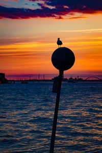 Silhouette pole by sea against sky during sunset