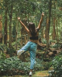 Rear view of woman with arms raised dancing on footpath in forest