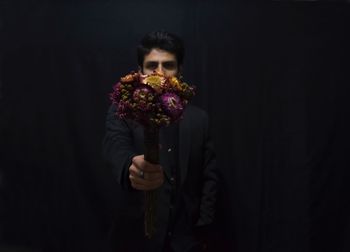 Close-up of young woman holding flower over black background