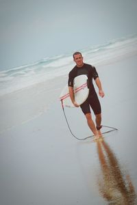 Tilt image of man walking with surfboard on wet shore