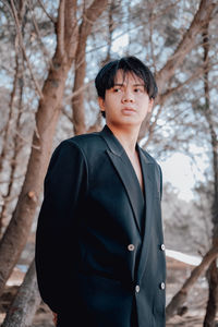 Young man standing by bare trees in forest