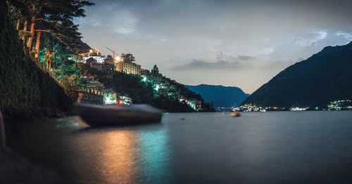 Illuminated buildings by sea against sky in city