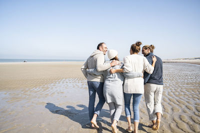Friends standing on beach against clear sky