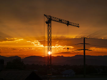 Silhouette cranes at construction site against sky during sunset