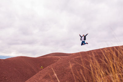 Full length of man jumping in desert against cloudy sky