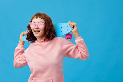 Portrait of young woman drinking water against blue background