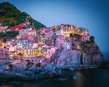 Illuminated townscape by sea against clear sky at dusk