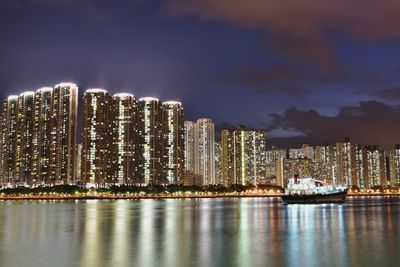 Illuminated buildings by sea against sky at night