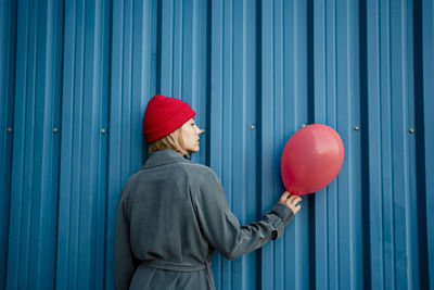 Mid adult woman holding red balloon by blue shutter