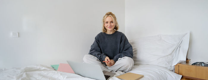 Portrait of young woman sitting on bed at home