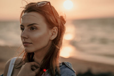 Portrait of young woman looking away against sky during sunset