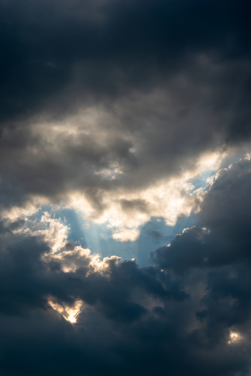 LOW ANGLE VIEW OF SUNLIGHT STREAMING THROUGH CLOUDS IN SKY