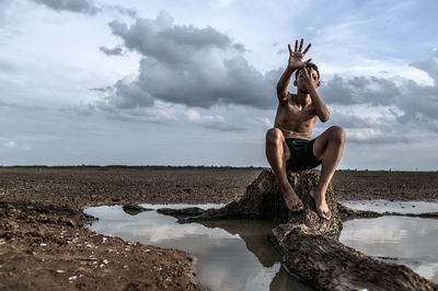 Sad boy sitting on rock by sea against cloudy sky