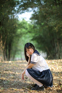 Full length of woman looking away while crouching on field