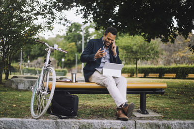 Full length of male freelancer talking on smart phone while sitting in park