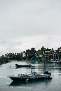 Boats in river by buildings in city against sky