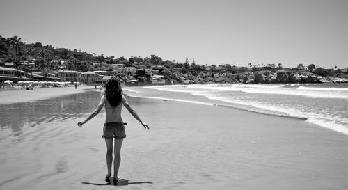 Rear view of woman walking on beach against clear sky