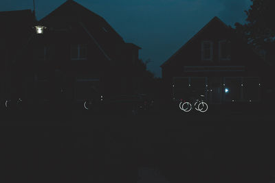 Silhouette buildings by street against sky at night