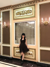 Full length portrait of woman standing against glass