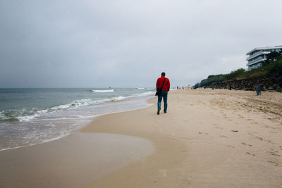 Rear view of men on beach against sky